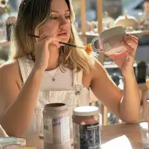 ruyagezisi.info  seramik atölyesinde, genç bir kadın el yapımı seramik kupayı özenle fırça ile boyuyor, sanatsal üretim sürecini sergiliyor.